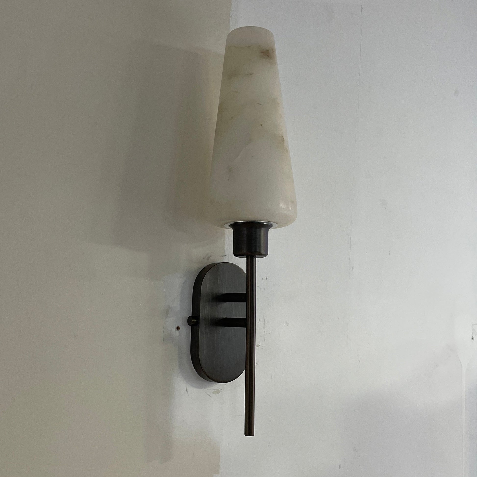 The Arras Wall Lamp shown in a bedroom setting above a nightstand.