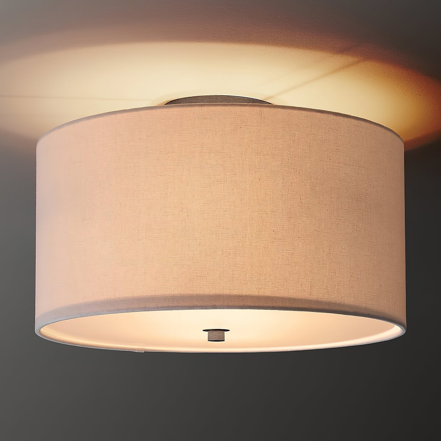 Harrison drum flush mount light illuminated, casting a warm glow in a bedroom.