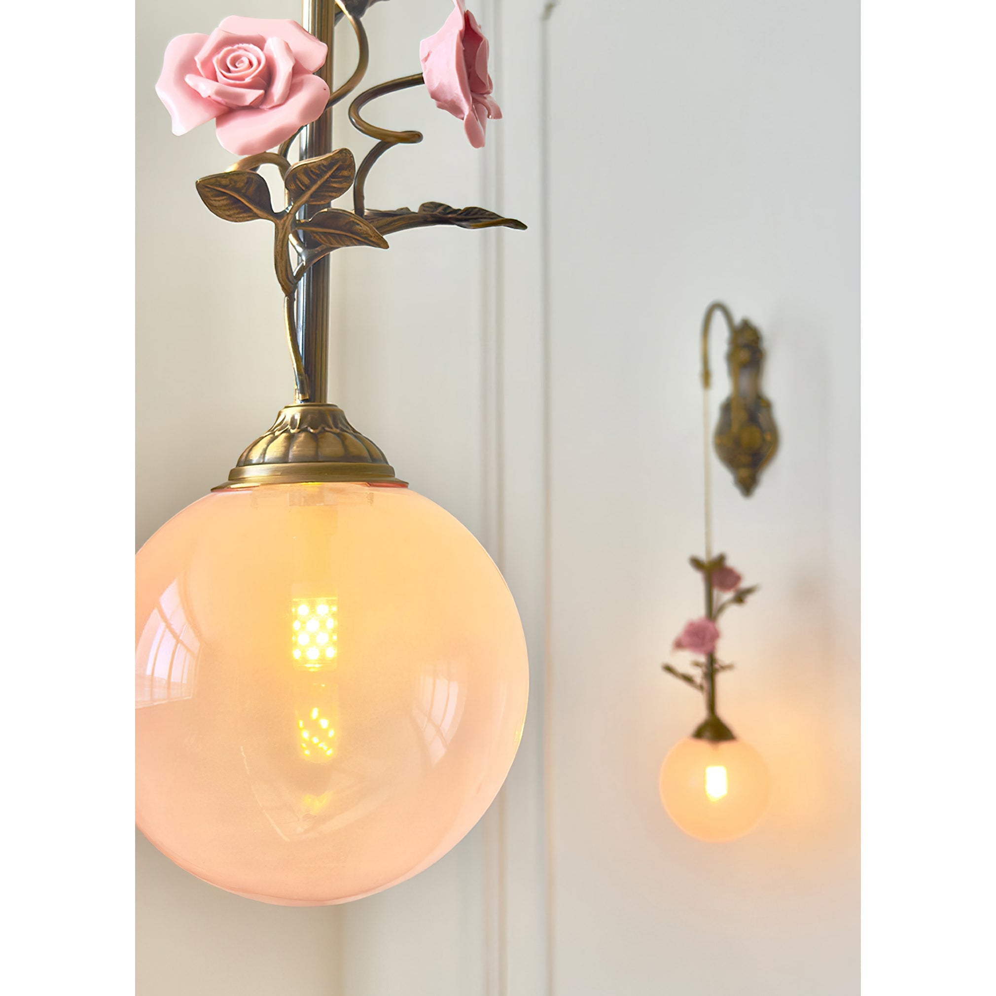 The pink glass rose sconce, illuminated, casting a warm glow.