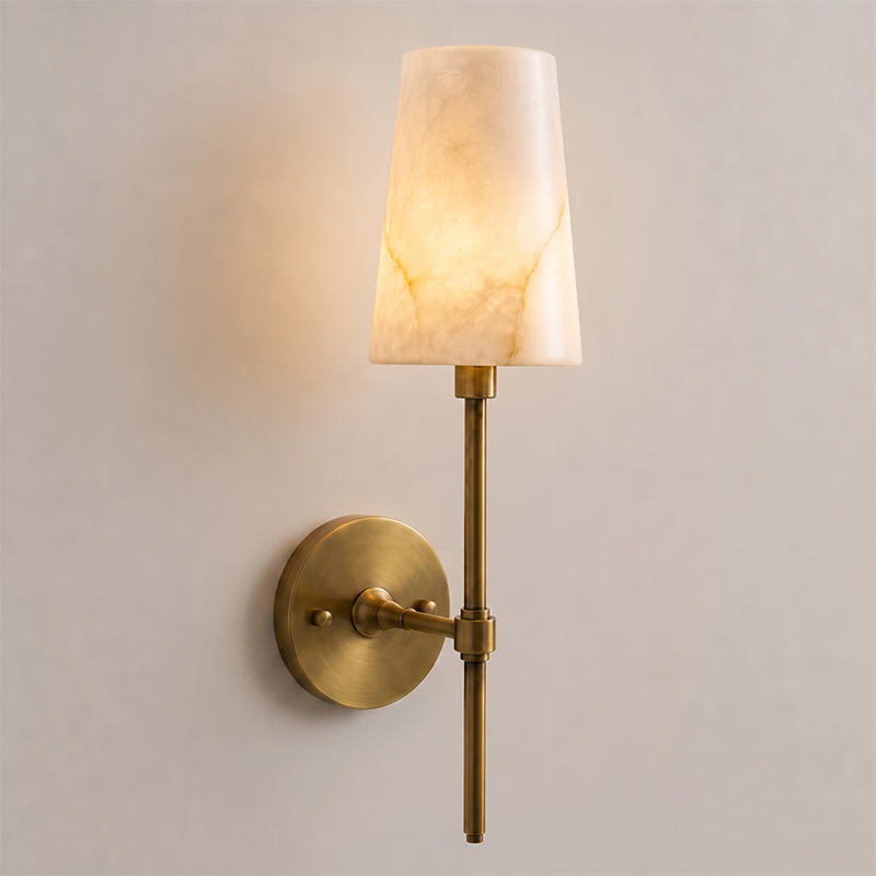 The brass backplate and hardware of the Hillsdale wall sconce against a wall.