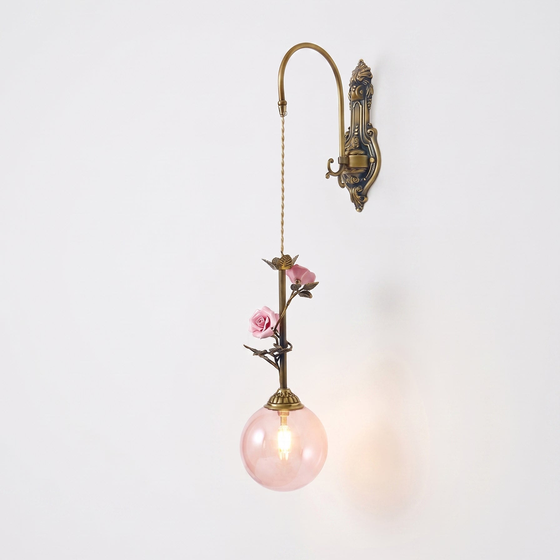 The clear glass rose sconce, lit, with light shining through.