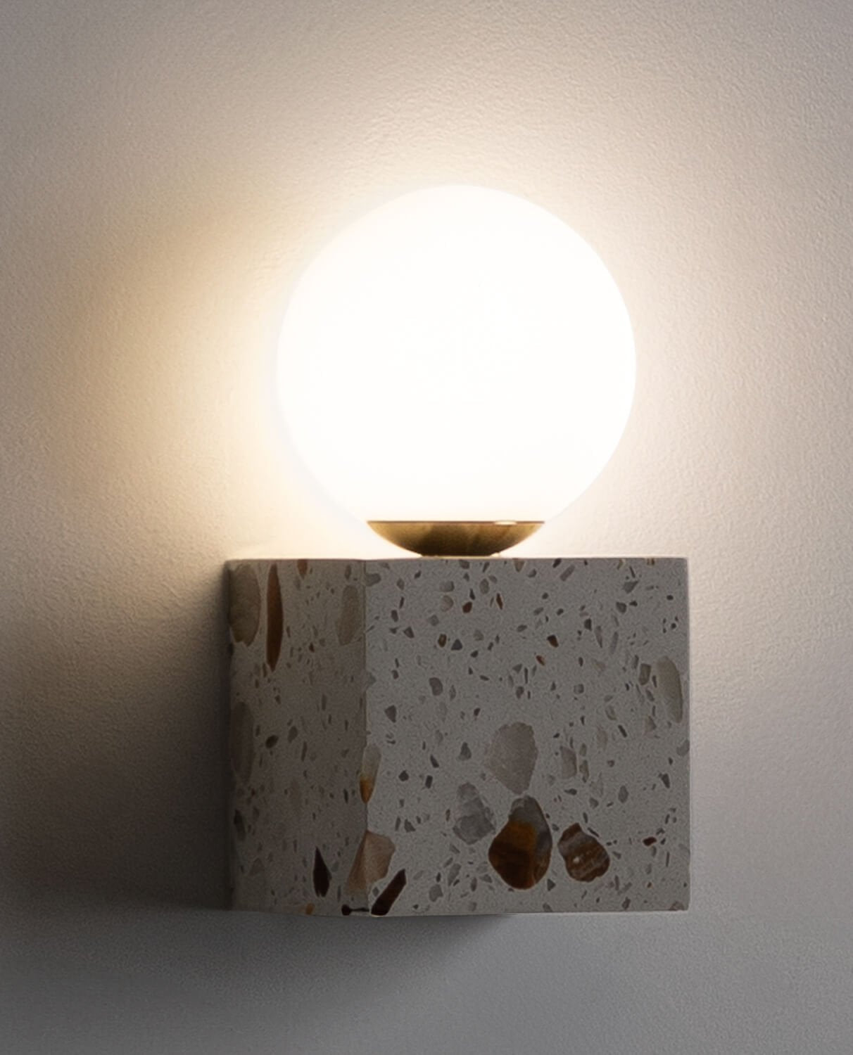 The cube wall sconce illuminated, casting a warm light against a wall.