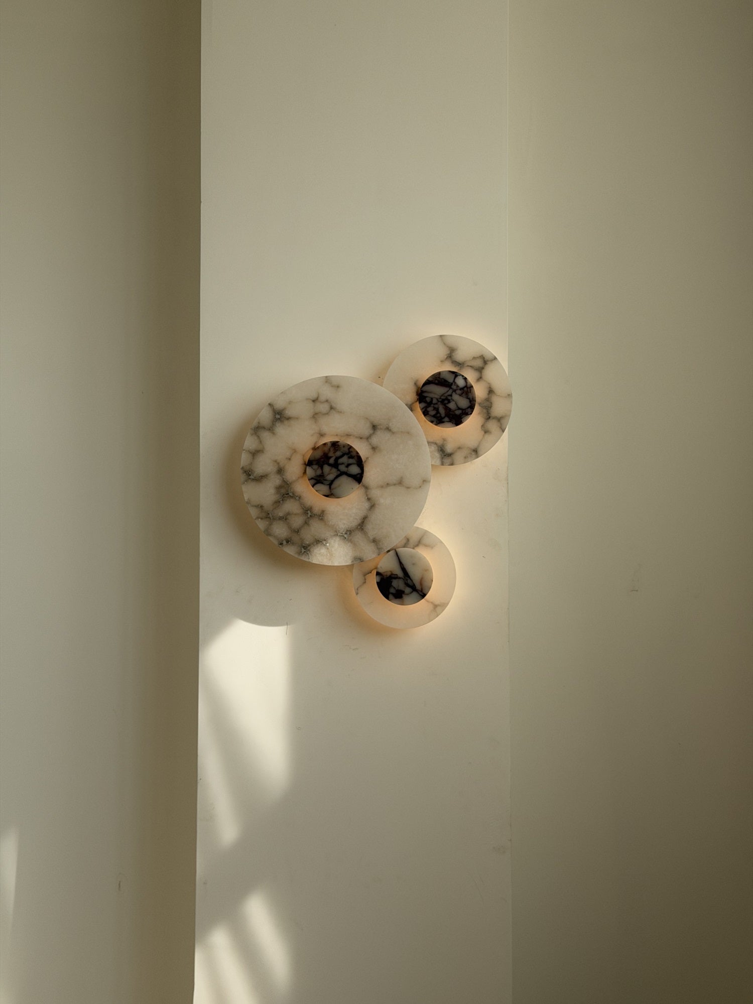 White Median Wall Lamp, illuminated, casting a warm glow.