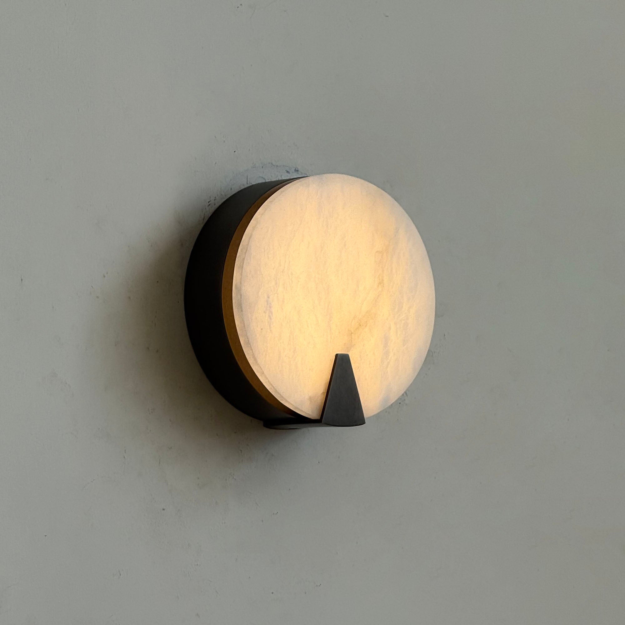 The sconce illuminated, casting a warm, inviting glow through the alabaster.