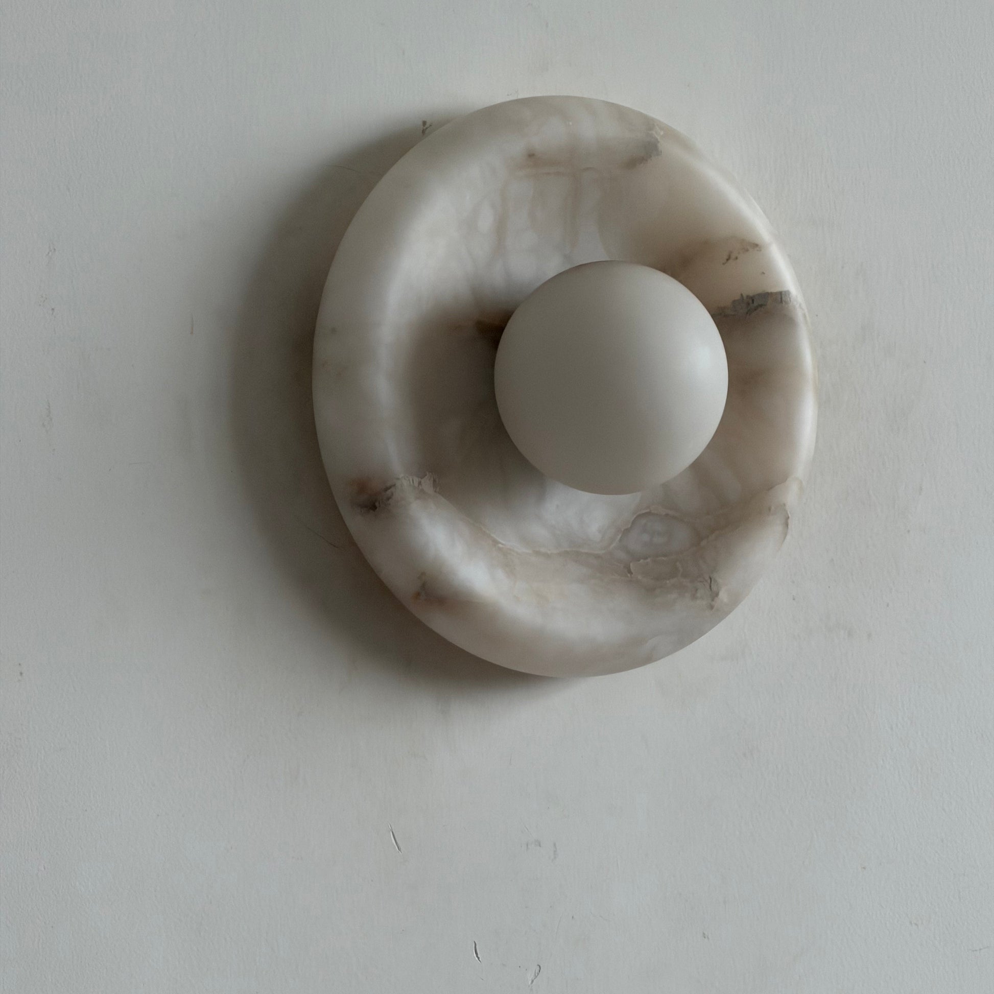 A pair of Orli Alabaster Wall Lamps flanking a piece of art.
