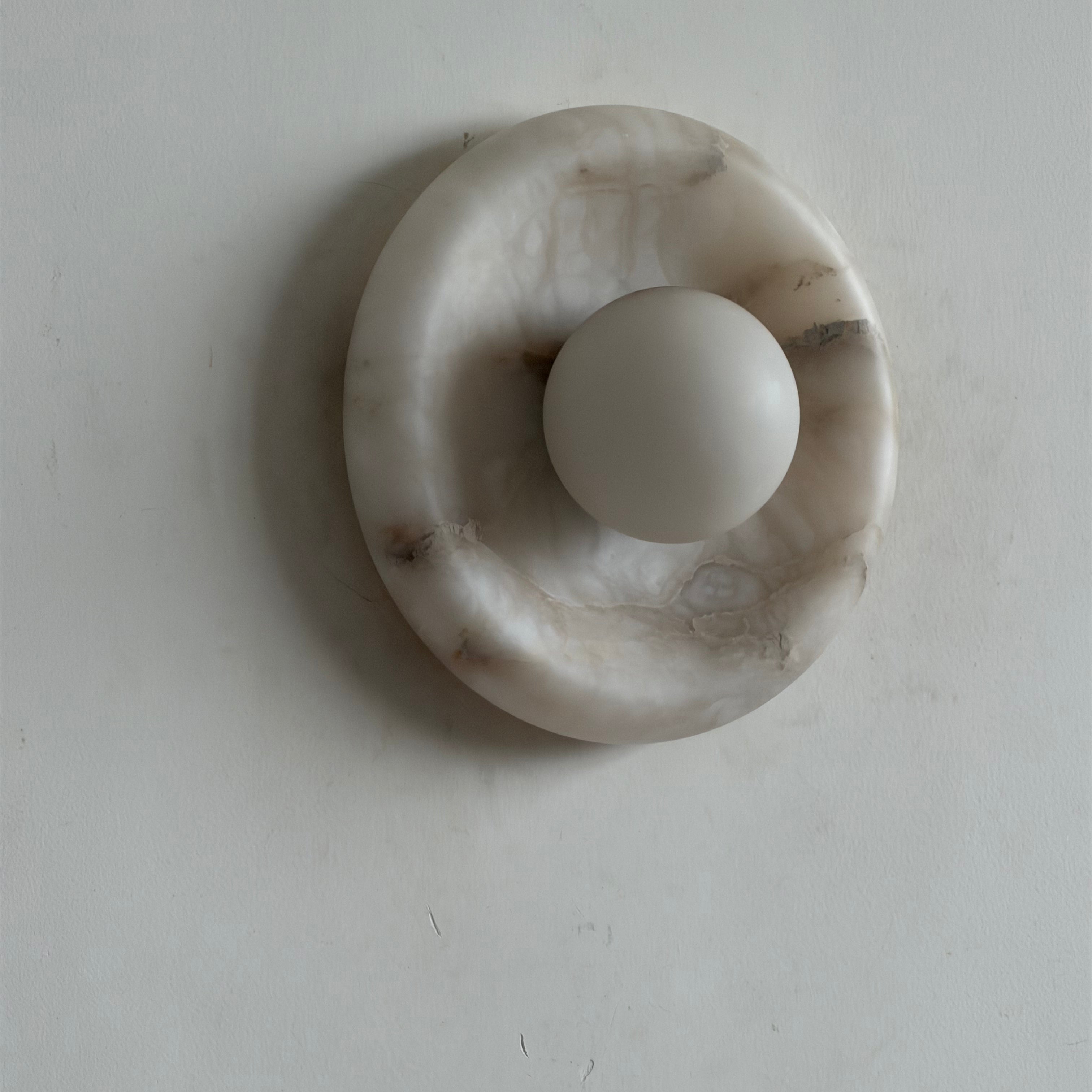 A pair of Orli Alabaster Wall Lamps flanking a piece of art.