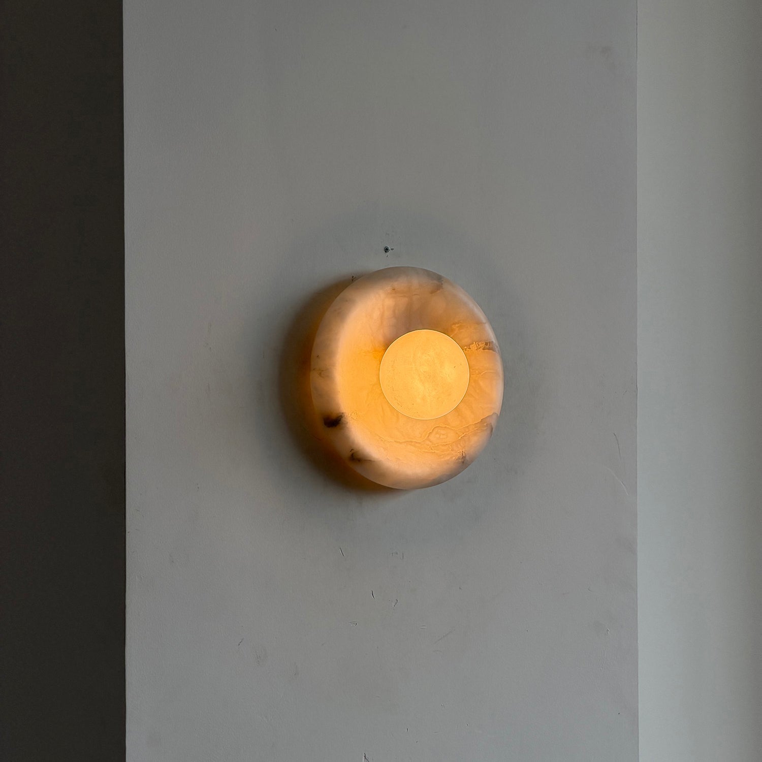 White Orli Wall Lamp against a dark, textured wall.