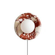 Front view of the Orli red marble plug-in sconce with its glass globe.