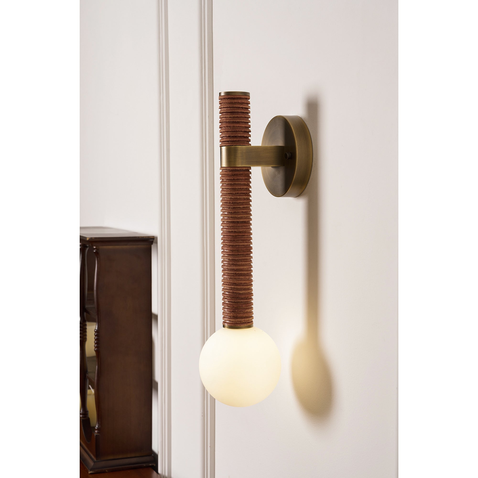 The Threadline sconce with a brown leather finish against a neutral wall.