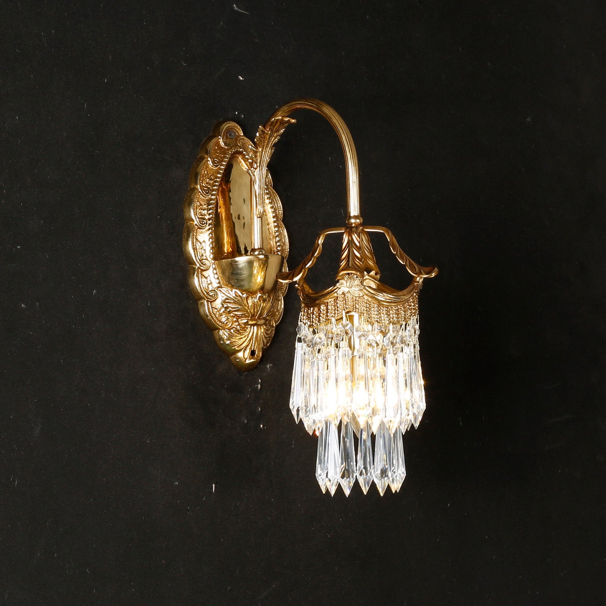 The ornate, traditional design of the sconce's brass backplate.
