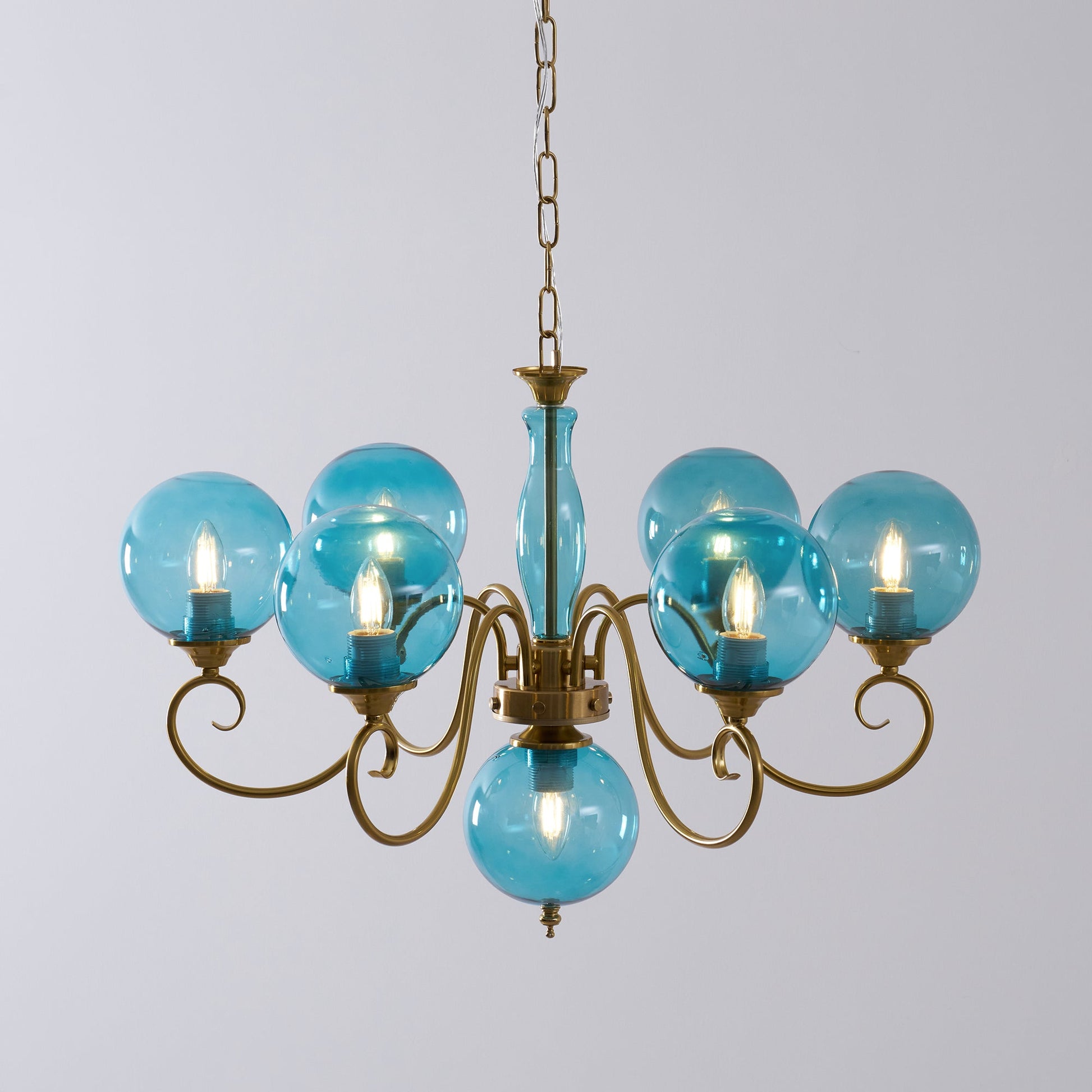The chandelier hanging in a room with high ceilings and large windows.