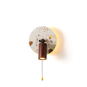 Swizzle Wall Lamp with terrazzo-style stone backplate, shown lit.