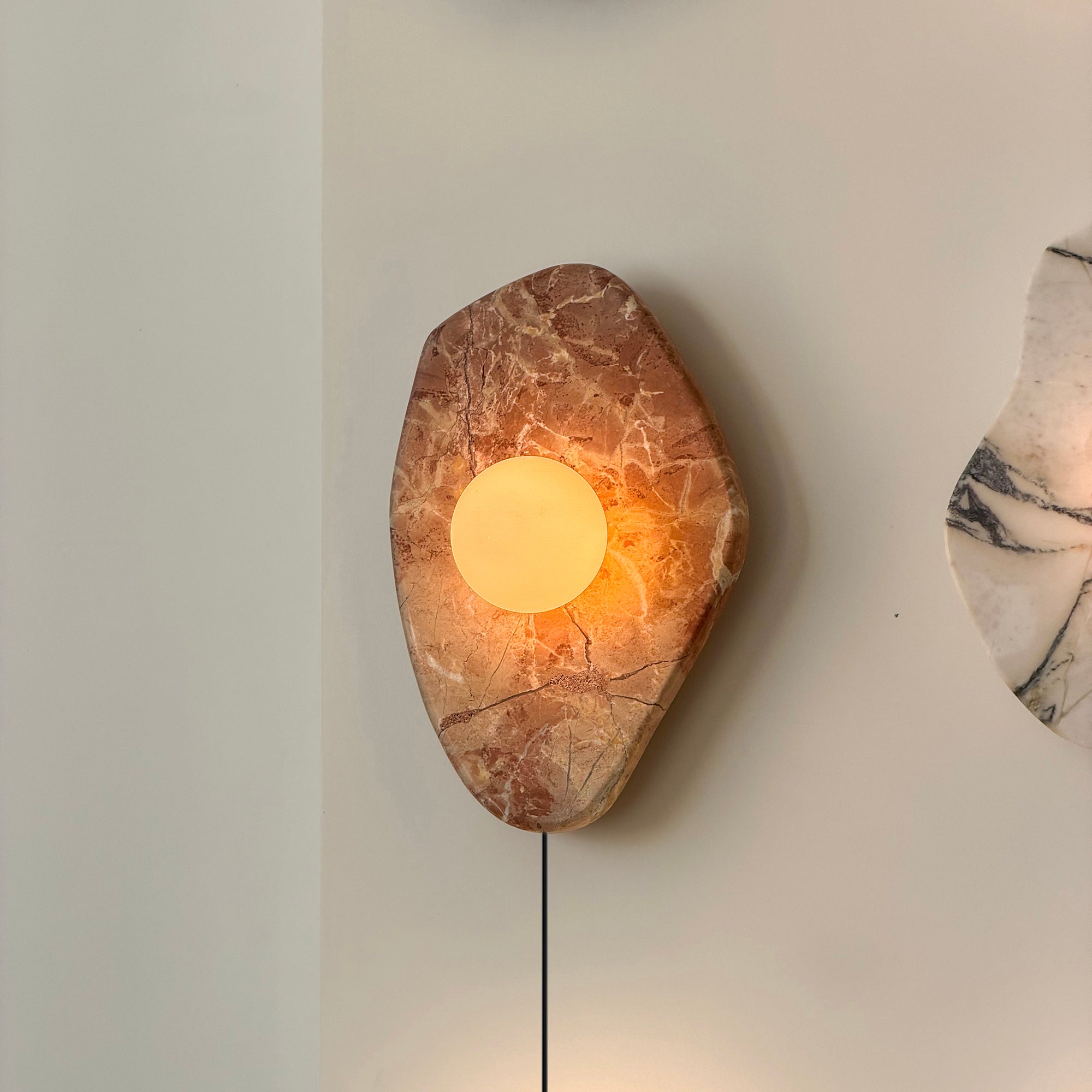 Angled view of the pink marble and glass wall lamp.